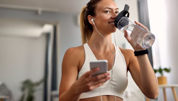 happy-sportswoman-using-smart-phone-while-having-water-break-living-room